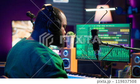 Talented famous composer writes down new verses and lyrics in home studio, composing music with digital software. Artist songwriter works with audio equipment and gear, recording tracks. Camera A. 119837508