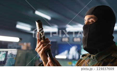Portrait of terrorist loading gun, attacking enemy command center. Close up of masked insurgent reloading pistol during enemy base assault hijacking in guerilla warfare armed conflict, camera B Portrait of terrorist loading gun, attacking enemy command center. Close up of masked insurgent reloading pistol during enemy base assault hijacking in guerilla warfare armed conflict, camera B 119837609