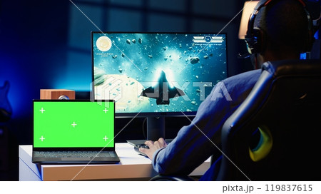 Mockup laptop on desk next to man playing SF videogame on computer, talking into headset with friends. Isolated screen notebook and gamer using headphones to chat with Esports team in game Mockup laptop on desk next to man playing SF videogame on computer, talking into headset with friends. Isolated screen notebook and gamer using headphones to chat with Esports team in game 119837615