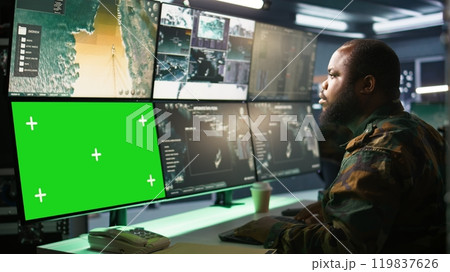 Military agent working in control room, using software on green screen devices, analyzing aerial reconnaissance data. Intelligence corps expert controlling drones with chroma key systems, camera B Military agent working in control room, using software on green screen devices, analyzing aerial reconnaissance data. Intelligence corps expert controlling drones with chroma key systems, camera B 119837626