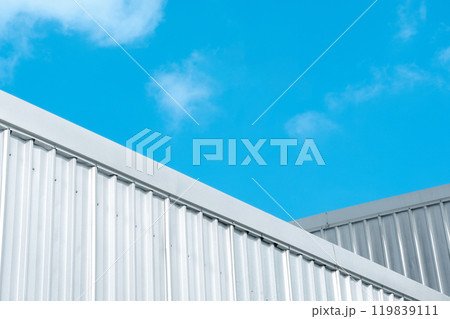 Industrial warehouse factory buildings with silver corrugated steel wall against blue sky background, low angle view. Industrial warehouse factory buildings with silver corrugated steel wall against blue sky background, low angle view. 119839111