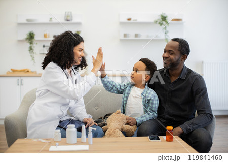 Cheerful doctor high fives young boy at home with dad 119841460