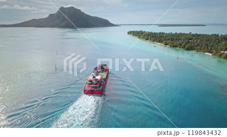 Big red cargo ship sailing to tropical island with turquoise lagoon. Water deliver bulk carrier to exotic remote places, Maupiti, French Polynesia. Export and import. Aerial view, drone flight 119843432