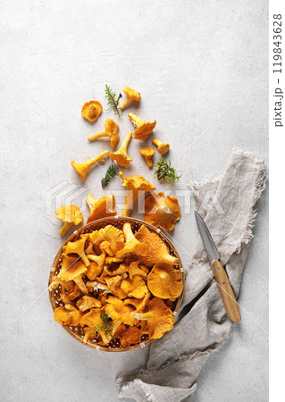 Top view of a bowl full of chanterelle mushrooms (Cantharellus cibarius). The bowl is on a gray background with a few more mushrooms. Top view of a bowl full of chanterelle mushrooms (Cantharellus cibarius). The bowl is on a gray background with a few more mushrooms. 119843628