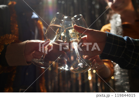 Cropped shot of people clinking glasses of champagne standing in top light while celebrating Christmas with silver tinsel in background at home party, copy space Cropped shot of people clinking glasses of champagne standing in top light while celebrating Christmas with silver tinsel in background at home party, copy space 119844015