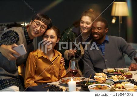 Candid shot of Asian man taking selfie with four cheerful friends while sitting at festive dining table celebrating Christmas at home party, copy space 119844072