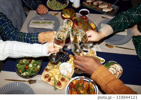 Cropped shot of people raising toast clinking glasses with champagne while celebrating Christmas together against dining table set with festive dishes, camera flash, copy space Cropped shot of people raising toast clinking glasses with champagne while celebrating Christmas together against dining table set with festive dishes, camera flash, copy space 119844121