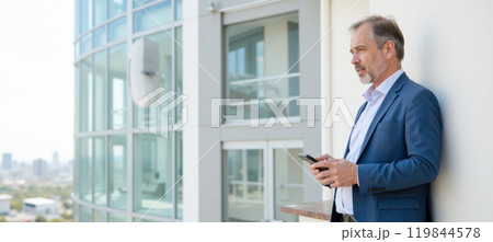 Mature man in blue blazer using smartphone near modern office building, city background, professional male with digital device, ample copy space on left side, urban setting, business attire 119844578
