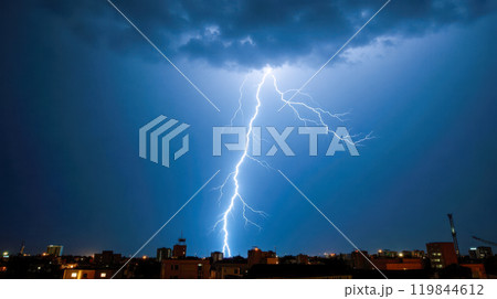 nighttime thunderstorm over cityscape, bright lightning bolt illuminating dark sky above skyscrapers, electric weather event in urban setting, powerful storm showcasing dramatic contrast 119844612