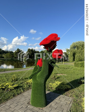 Artistic Green Hand Sculpture Holding Bright Red Flowers in a Scenic Park 119846244