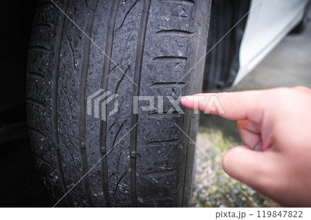 A hand pointing to worn out a car tire tread 119847822