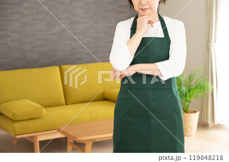 家のリビングで悩む緑のエプロンをしたシニア女性の主婦・家政婦 119848218