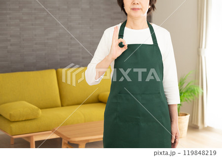 家のリビングで丸サインをする緑のエプロンをしたシニア女性の主婦・家政婦 119848219
