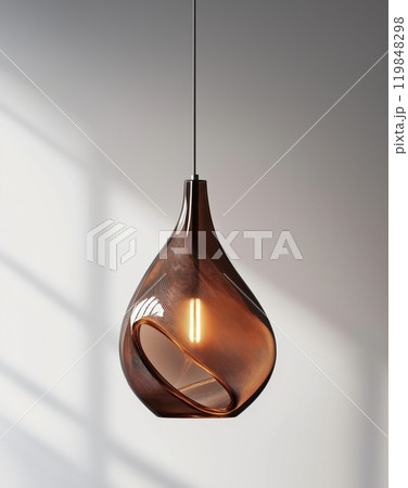 Elegant amber glass pendant light with a sculptural design, casting a soft glow on a neutral wall 119848298