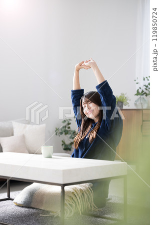 リビングのソファに座って伸びをする若い女性　遅く起きた冬の朝のリラックス 119850724