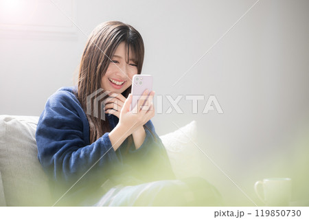 ソファーでスマホを見る若い女性　笑顔でスマホをを見る　嬉しい楽しい表情の秋冬 119850730