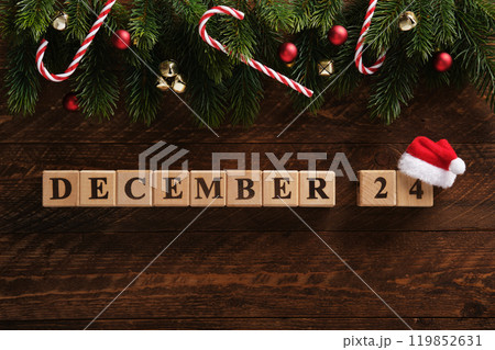 Date December 24 on a dark wooden background with fir sprigs, Christmas tree balls, bells and sugar canes. Festive background. 119852631