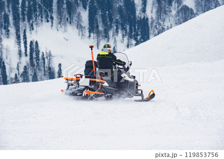 Rescuer man driving snowmobile on the ski resort. Rescuer man driving snowmobile on the ski resort. 119853756