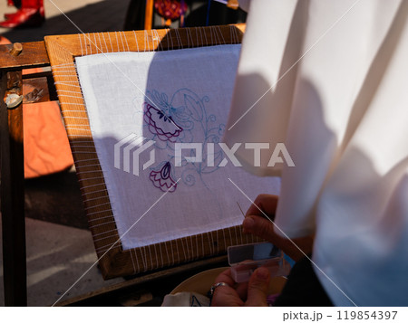 close-up shot of a woman from behind embroidering a flower on a white framed canvas 119854397