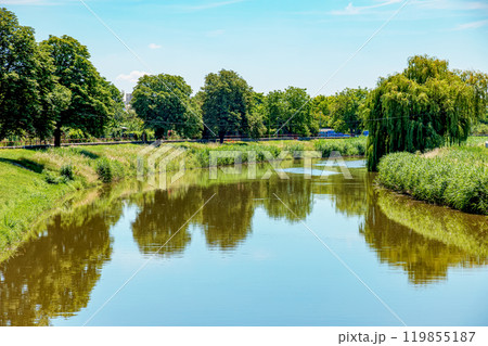 The river flows through the city. On the calm surface of the river banks are reflected. Slovak river Nitra on a bright sunny day. 119855187