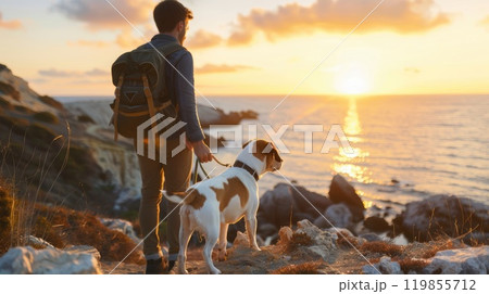 A man and his dog are walking along a rocky beach at sunset A man and his dog are walking along a rocky beach at sunset 119855712