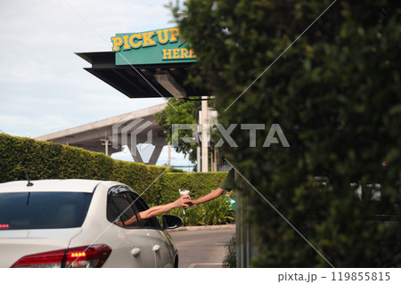 Hand Man in car receiving coffee in drive thru fast food restaurant. Staff serving takeaway order for driver in delivery window. Drive through and takeaway for buy fast food for protect covid19. Hand Man in car receiving coffee in drive thru fast food restaurant. Staff serving takeaway order for driver in delivery window. Drive through and takeaway for buy fast food for protect covid19. 119855815