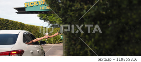 Hand Man in car receiving coffee in drive thru fast food restaurant. Staff serving takeaway order for driver in delivery window. Drive through and takeaway for buy fast food for protect covid19. 119855816