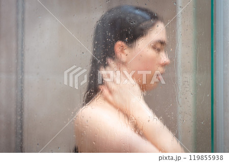 Side view of blurred Caucasian naked young woman taking a shower in modern grey bathroom. Daily hygiene routine and hair care Side view of blurred Caucasian naked young woman taking a shower in modern grey bathroom. Daily hygiene routine and hair care 119855938