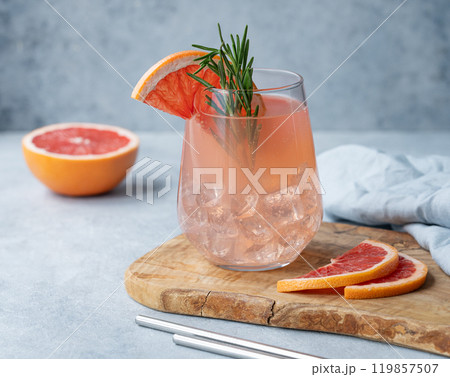 Homemade grapefruit lemonade with rosemary and ice in a glass on a wooden board on a blue background 119857507