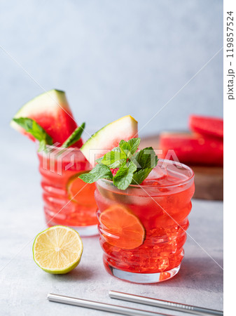 Two glasses watermelon cocktail with lime, ice and mint on a blue  background with fruits. Two glasses watermelon cocktail with lime, ice and mint on a blue  background with fruits. 119857524