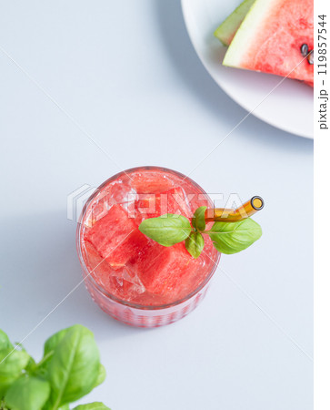 Glass of refreshing watermelon cocktail with basil and ice on a blue background with fresh herb 119857544