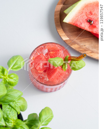 Glass of refreshing watermelon cocktail with basil and ice on a light background with fresh herb  119857547