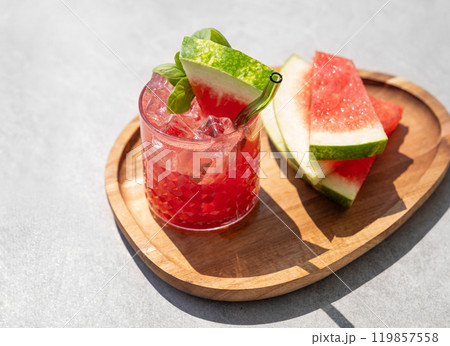Glass of refreshing watermelon cocktail with basil, ice on wooden board with fruit slices  119857558