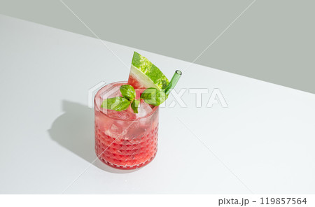 Glass of refreshing watermelon smoothie with basil, ice on white and green background with shadow. 119857564
