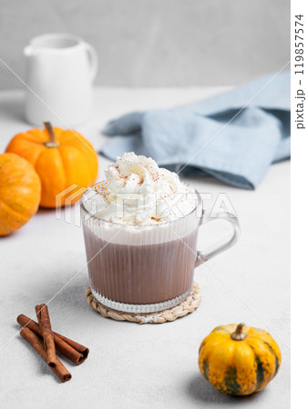 Hot chocolate with whipped cream in glass cup on light background with decorative pumpkins  119857574