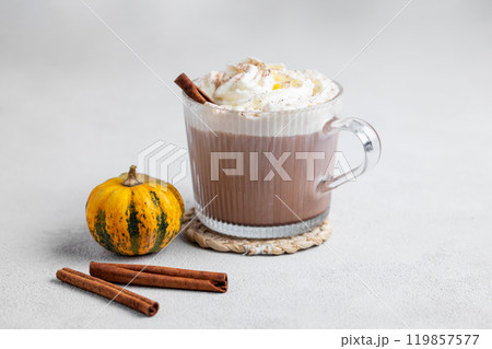 Spice latte or hot chocolate with whipped cream in glass cup on light background with  pumpkins 119857577