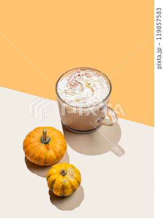 Spice latte with whipped cream in glass cup on orange background with decorative pumpkins and shadow Spice latte with whipped cream in glass cup on orange background with decorative pumpkins and shadow 119857583