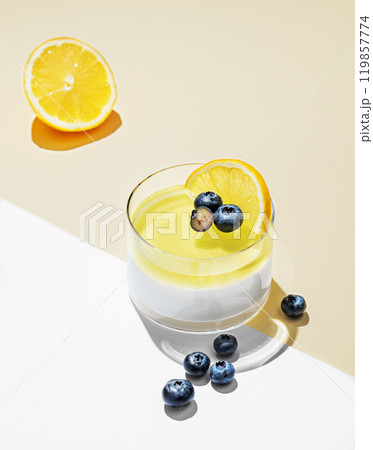 Creamy lemon panna cotta with blueberries in a glass on a yellow and white  background  119857774