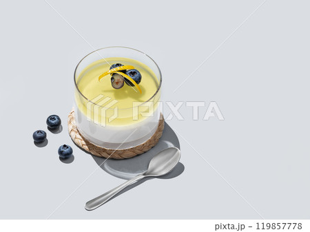 Lemon panna cotta with blueberries in a glass on a blue background with fresh berries, spoons 119857778