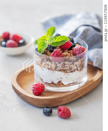Greek yogurt with muesli or granola, raspberries and blueberries in a glass on a wooden board  119857806