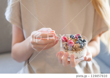 Granola with greek yogurt, raspberries and blueberries in a glass in hands of a woman 119857810