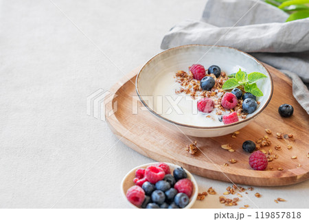 Granola with greek yogurt, raspberries and blueberries in a bowl on a wooden board  119857818