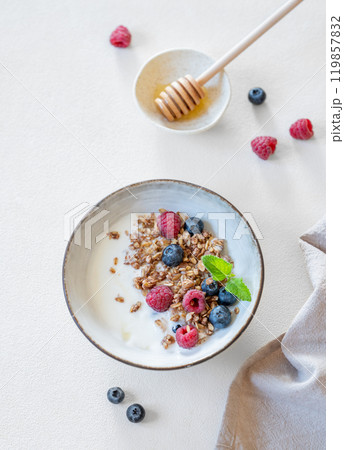 Flat lay of granola with yogurt, raspberries, blueberries and honey in a bowl on a white background 119857832