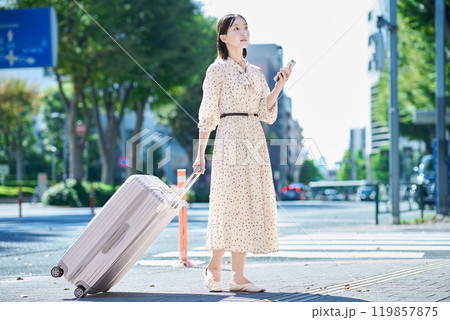 スーツケースとスマートフォンを持って街を歩く若い女性 119857875