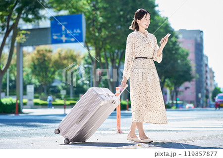 スーツケースとスマートフォンを持って街を歩く若い女性 スーツケースとスマートフォンを持って街を歩く若い女性 119857877