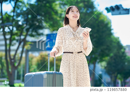 スーツケースとスマートフォンを持って街を歩く若い女性 119857880