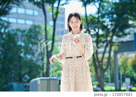 スーツケースとスマートフォンを持って街を歩く若い女性 スーツケースとスマートフォンを持って街を歩く若い女性 119857881
