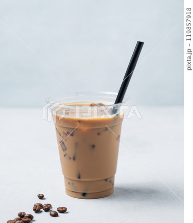 Iced coffee in a recyclable plastic glass with milk and ice on a light background with coffee beans. 119857918