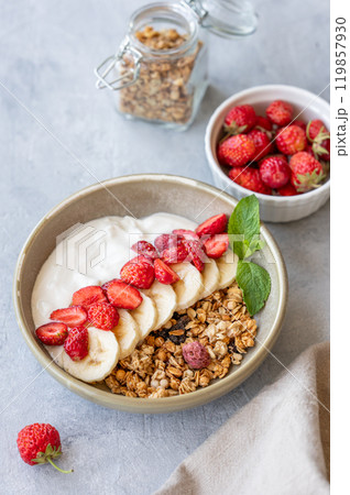 Natural greek yogurt with muesli, strawberry and banana in a bowl on a light background 119857930