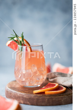 Homemade grapefruit lemonade with rosemary and ice in a glass on a wooden board on a blue background 119857945